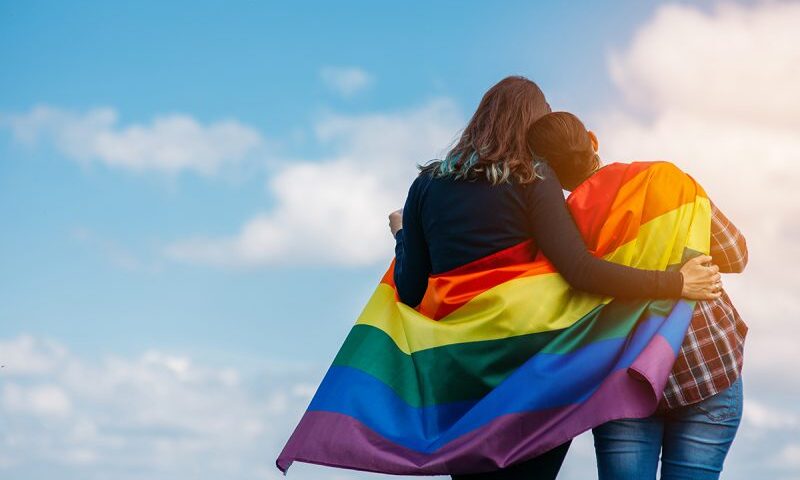 Two women hugging under rainbow flag