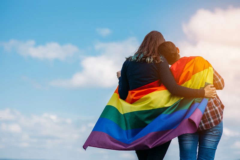 Two women hugging under rainbow flag