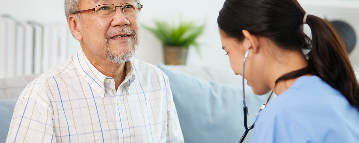 nurse or caregiver using stethoscope to examine senior man at home