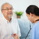 nurse or caregiver using stethoscope to examine senior man at home
